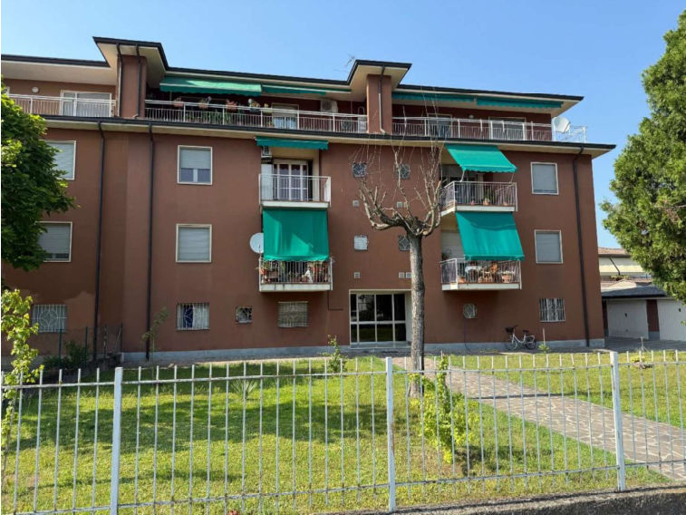 Immagine di un edificio residenziale plurifamiliare con balconi e tettoia, recinzione e area verde circostante.